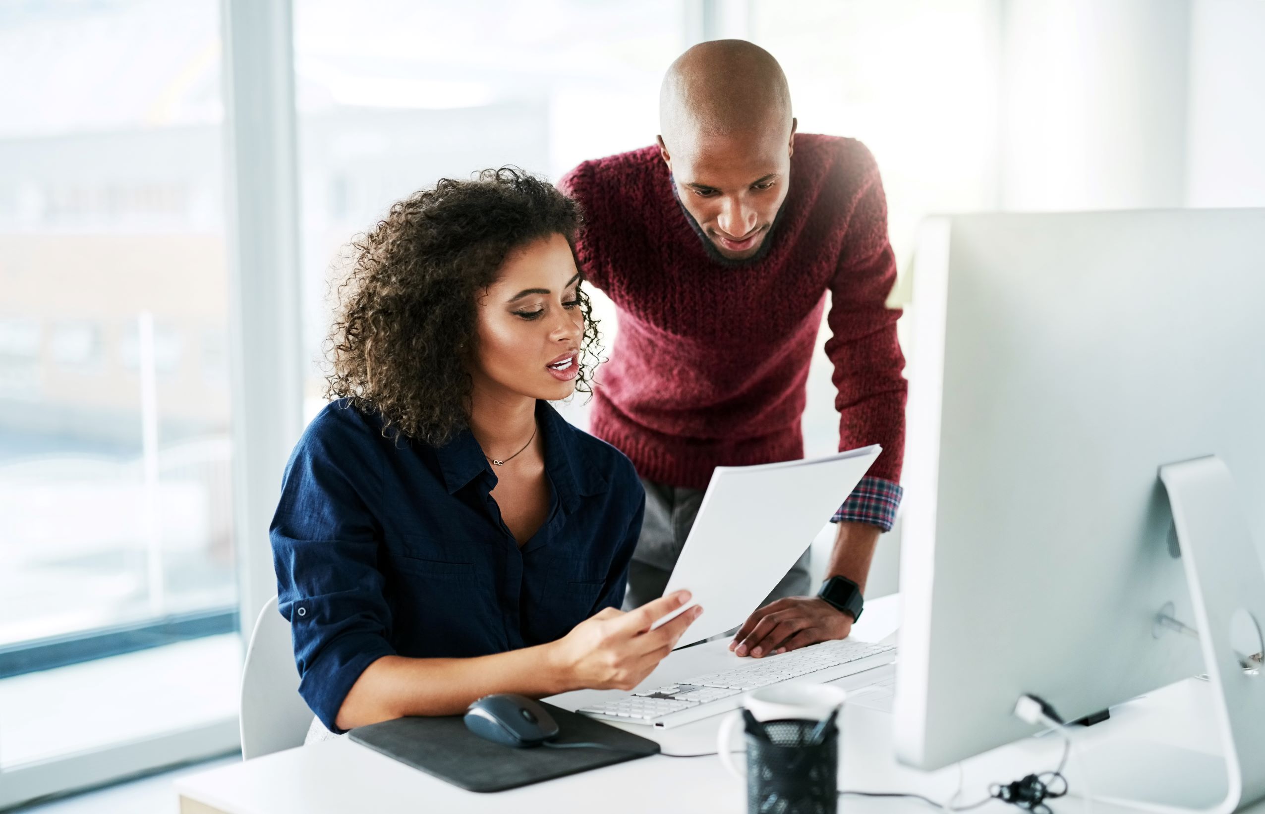 male leaning over at seated female's desk with both looking at papers