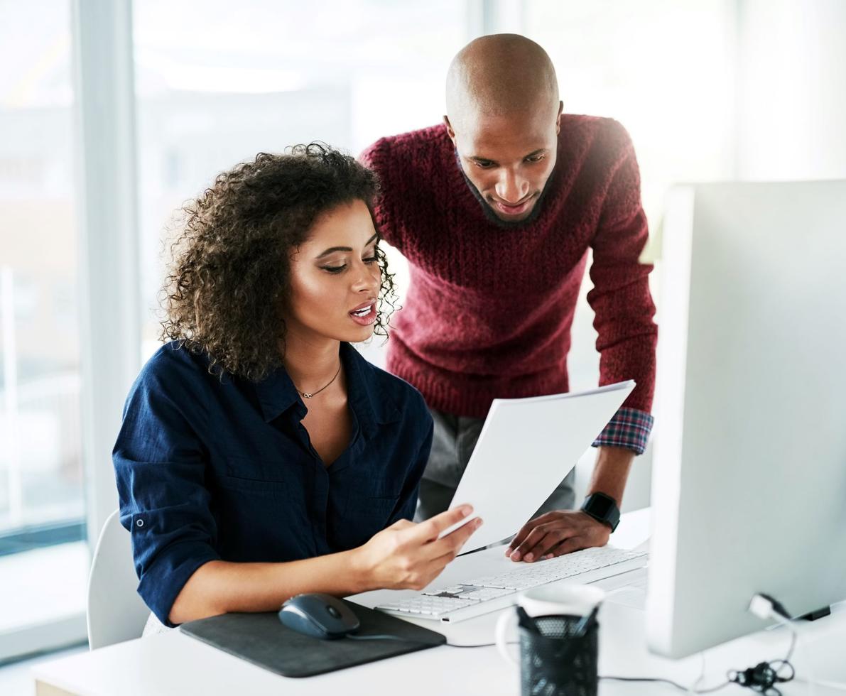 male leaning over at seated female's desk with both looking at papers