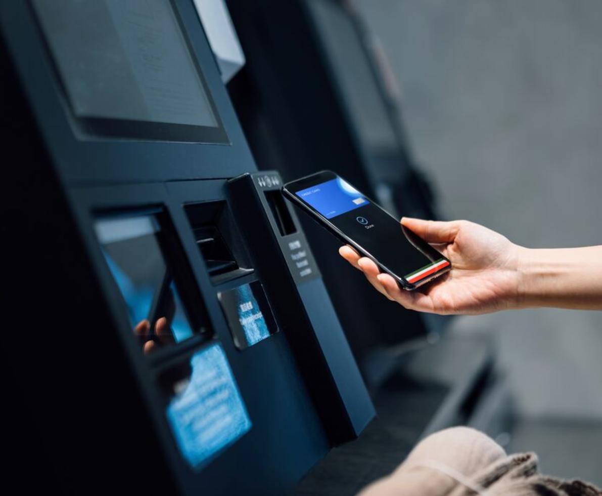 person holding smartphone in front of ATM machine